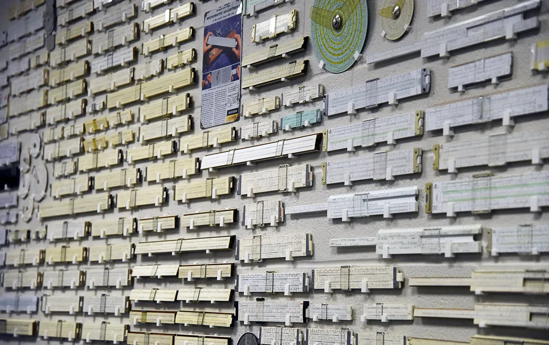 Jay's slide rule collection mounted on display across a classroom wall